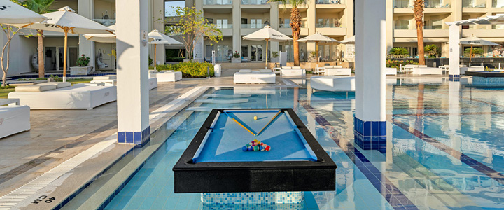 Ein Pool-Billardtisch steht im Wasser der modernen Poollandschaft des Steigenberger Pure Lifestyle. Im Hintergrund zeigt sich die stilvolle Hotelanlage.